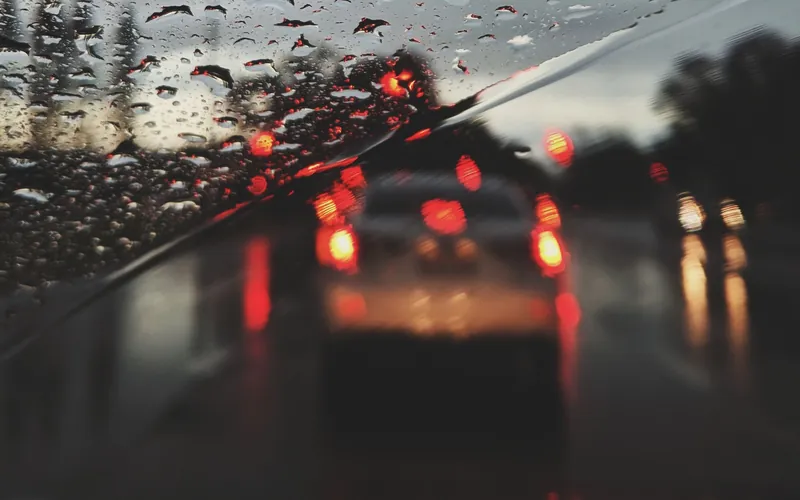 Blick durch eine regennasse Windschutzscheibe auf die Bremslichter des vorausfahrenden Fahrzeugs