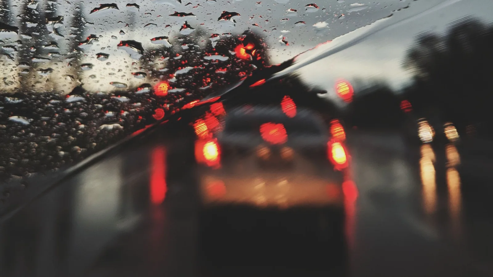 Blick durch eine regennasse Windschutzscheibe auf die Bremslichter des vorausfahrenden Fahrzeugs